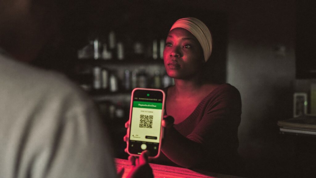Comerciante mostra o QR code de pagamento no celular ao cliente, no balcão de um pequeno comércio de bairro