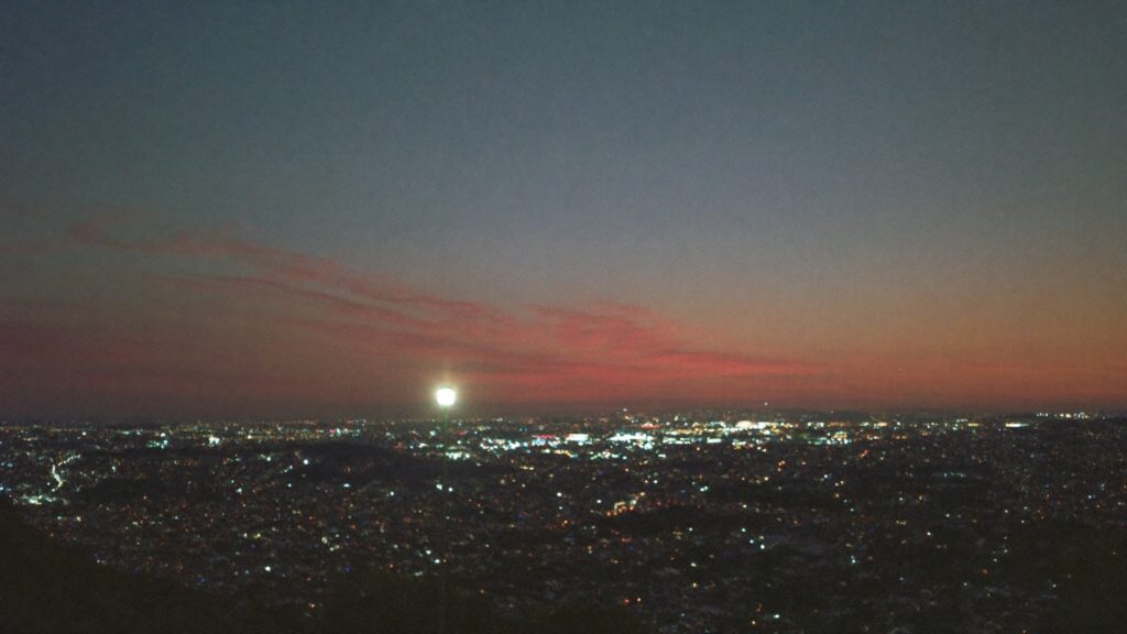 Vista de uma cidade brasileira ao anoitecer, com as luzes das casas se acendendo